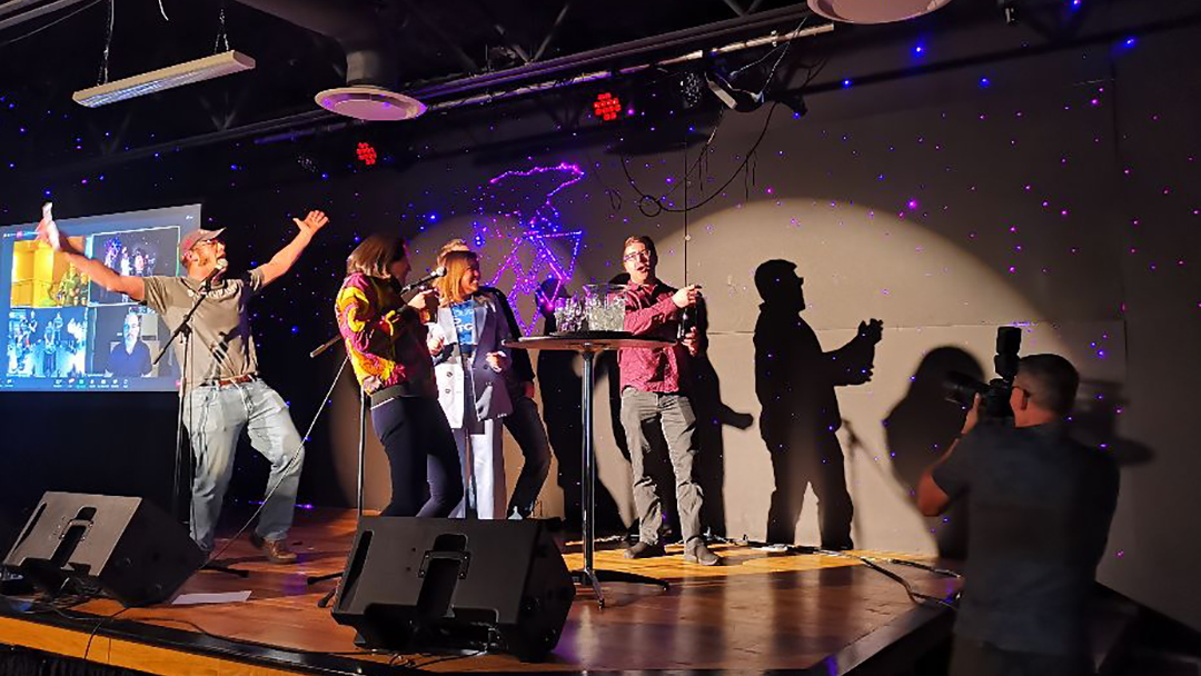 Nir Katchinskiy (right) of PulseMedica celebrates his win at the Startup TNT Investment Summit IV with a group of people, while host Zack Storms (left) exults.