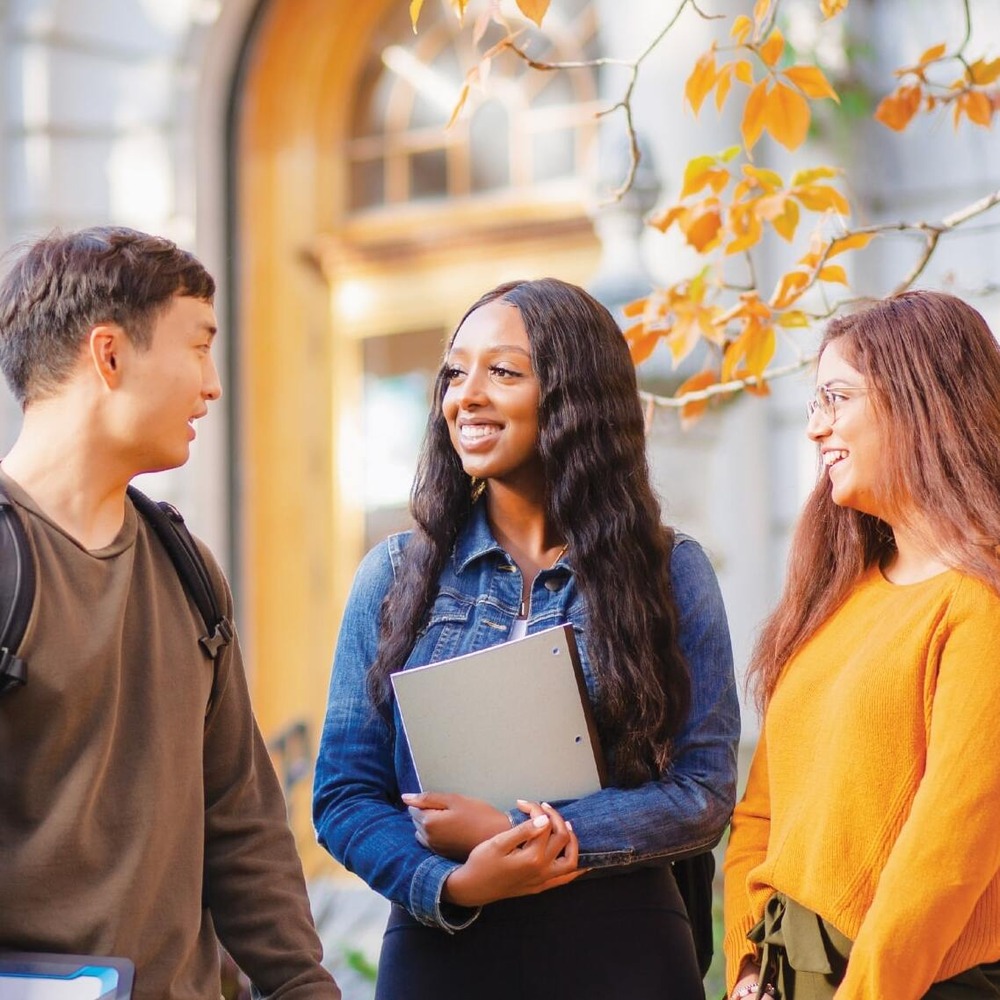 Students chat in front of the Old Arts Building on a bright fall day.