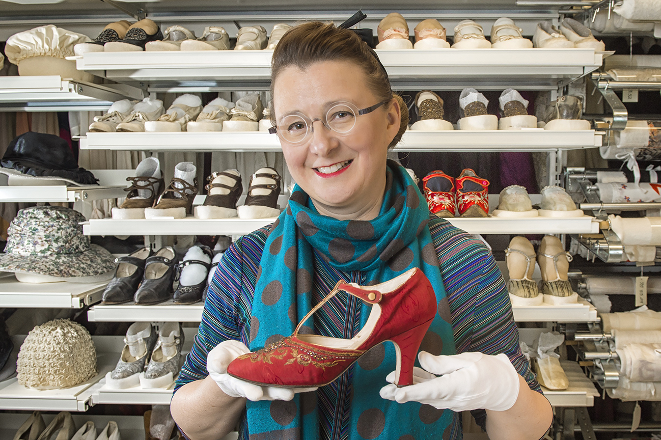 A woman holds a red shoe in front of a shelving system