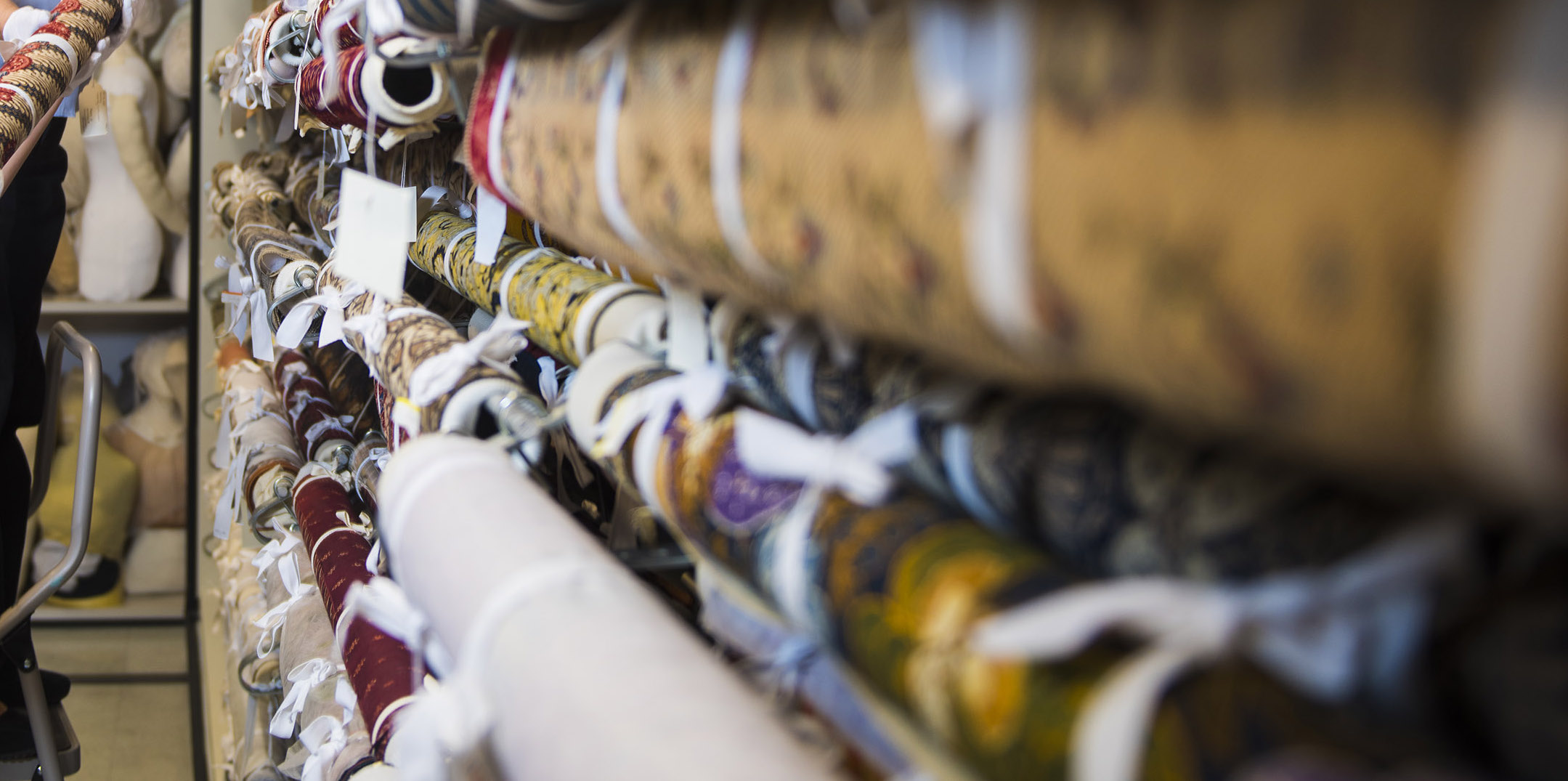 Rows of tightly rolled textiles tied with fabric sashes are horizontally stored on a wall.