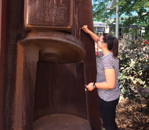 Jean faces a large sculpture while cleaning it with a small tool