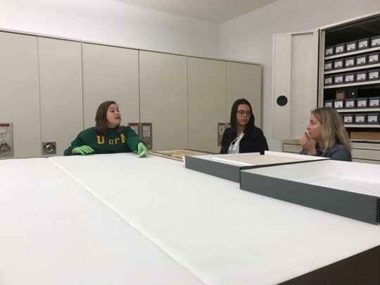 Three people stand around a white table with artifacts.