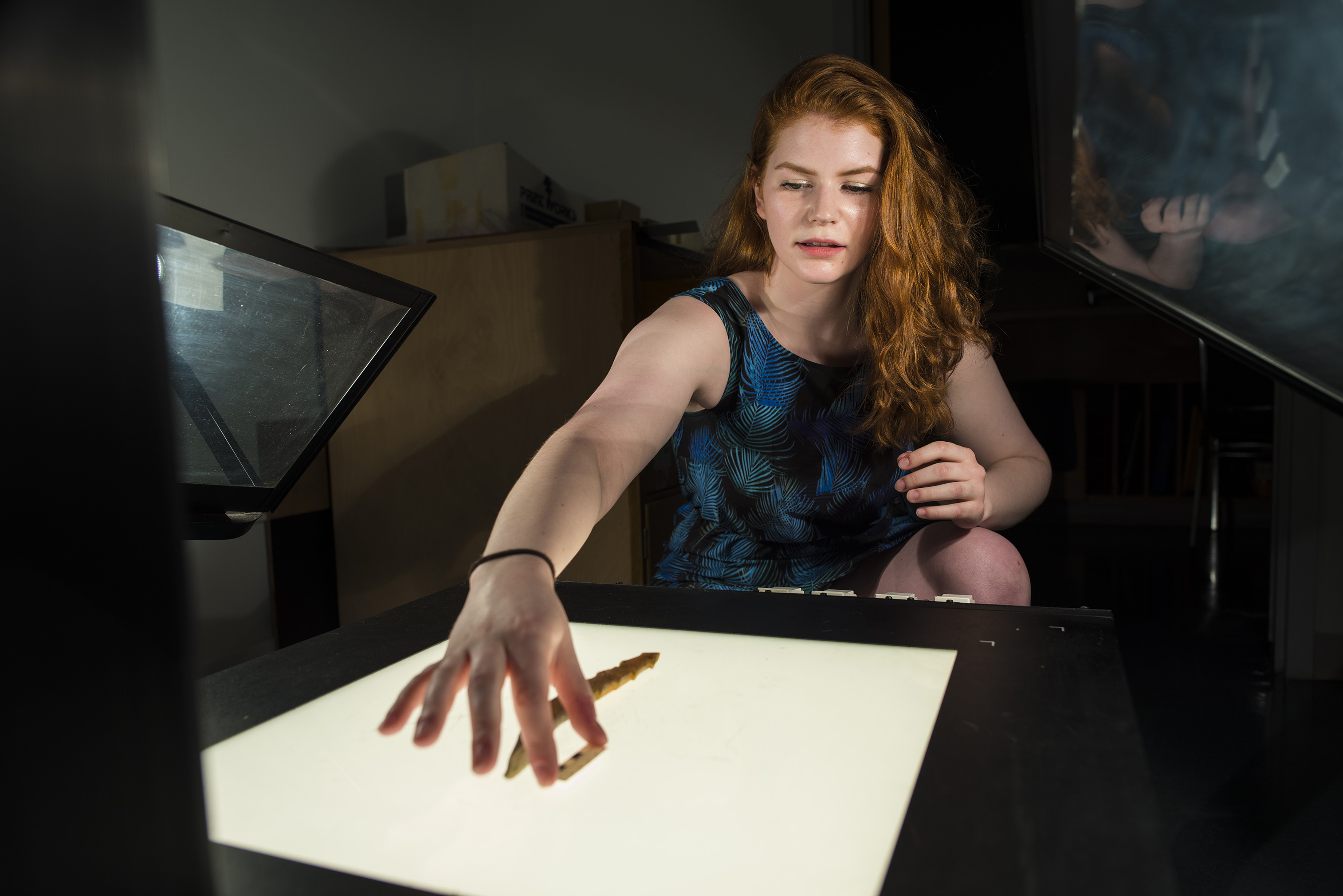 A volunteer arranges two small artifacts from the Bryan/Gruhn Archaeology collection on a bright table light