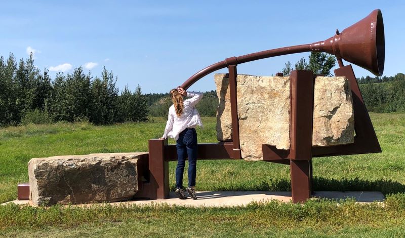 Girl with her ear up to a large metal sculpture