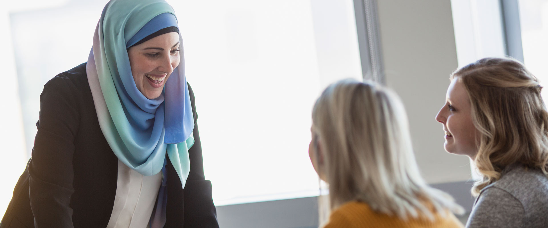 A female instructor (wearing an hijab) is smiling towards two female students