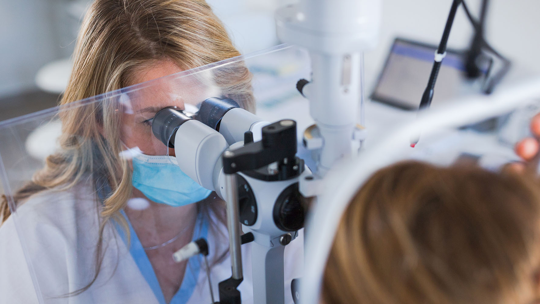 A healthcare professional conducts an eye examination using specialized optical equipment.