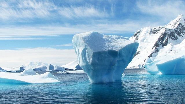 Ice berg floating in arctic ocean surrounded by ice caps