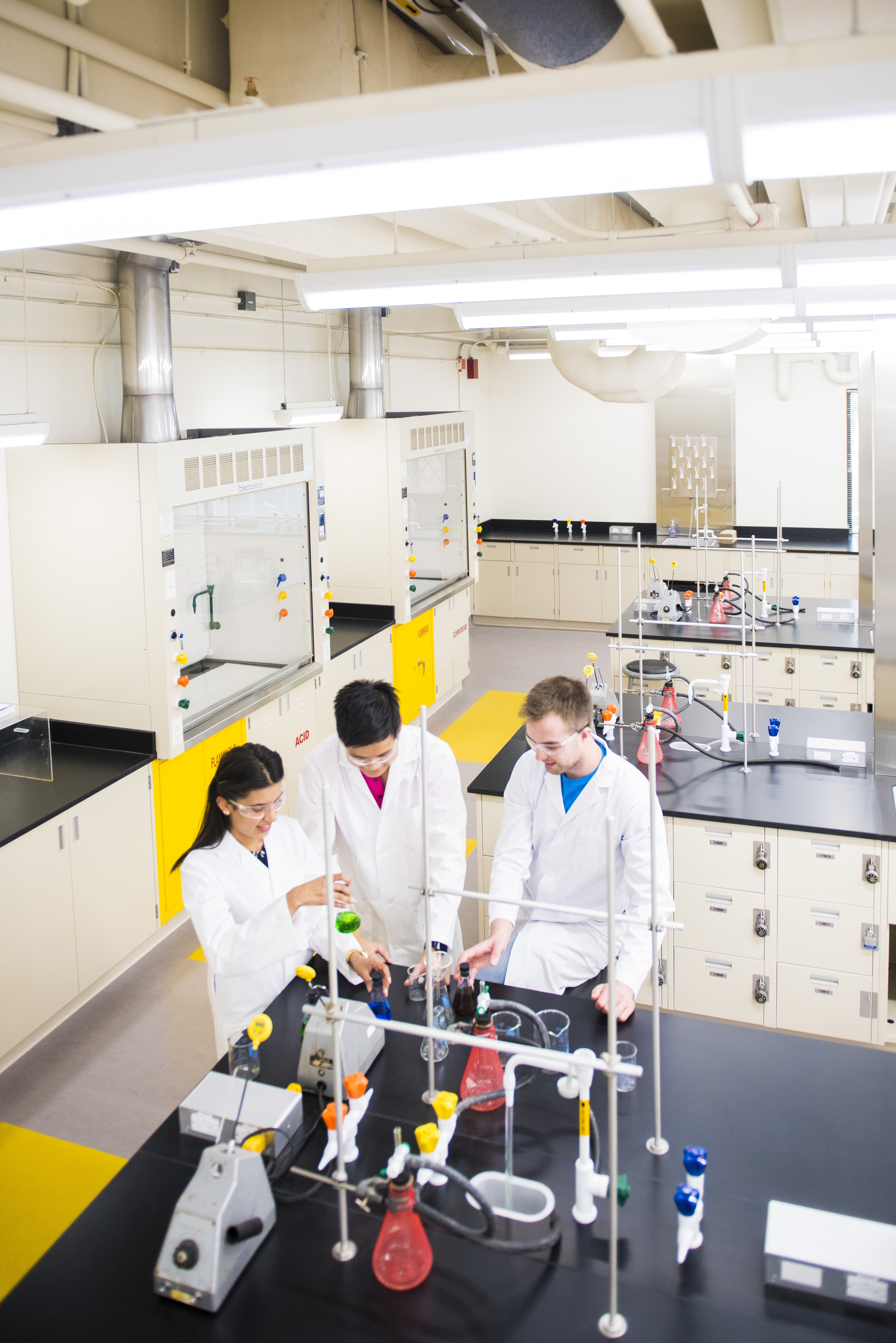 Students in a lab with chemicals and containers in front of them on a workbench.