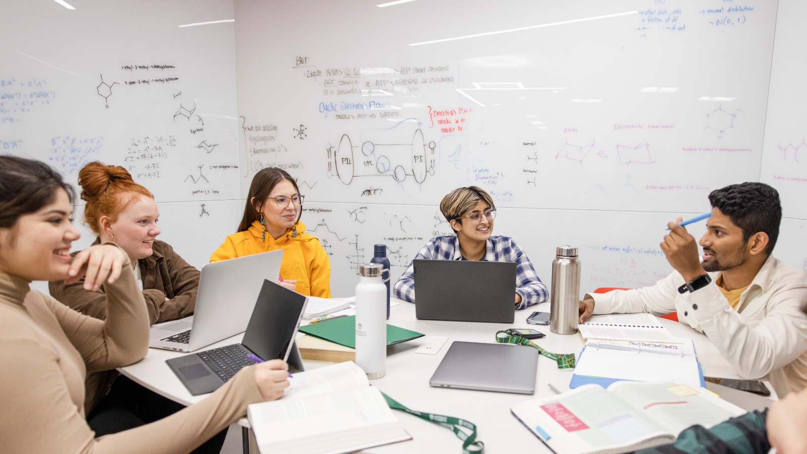 Students at a table discussing and interacting. A whiteboard with notes in the background.