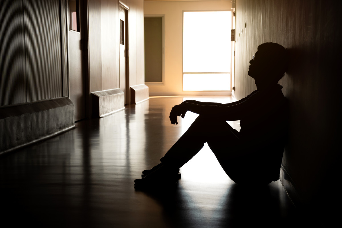 A person sits alone in a dark hallway, silhouetted by light.