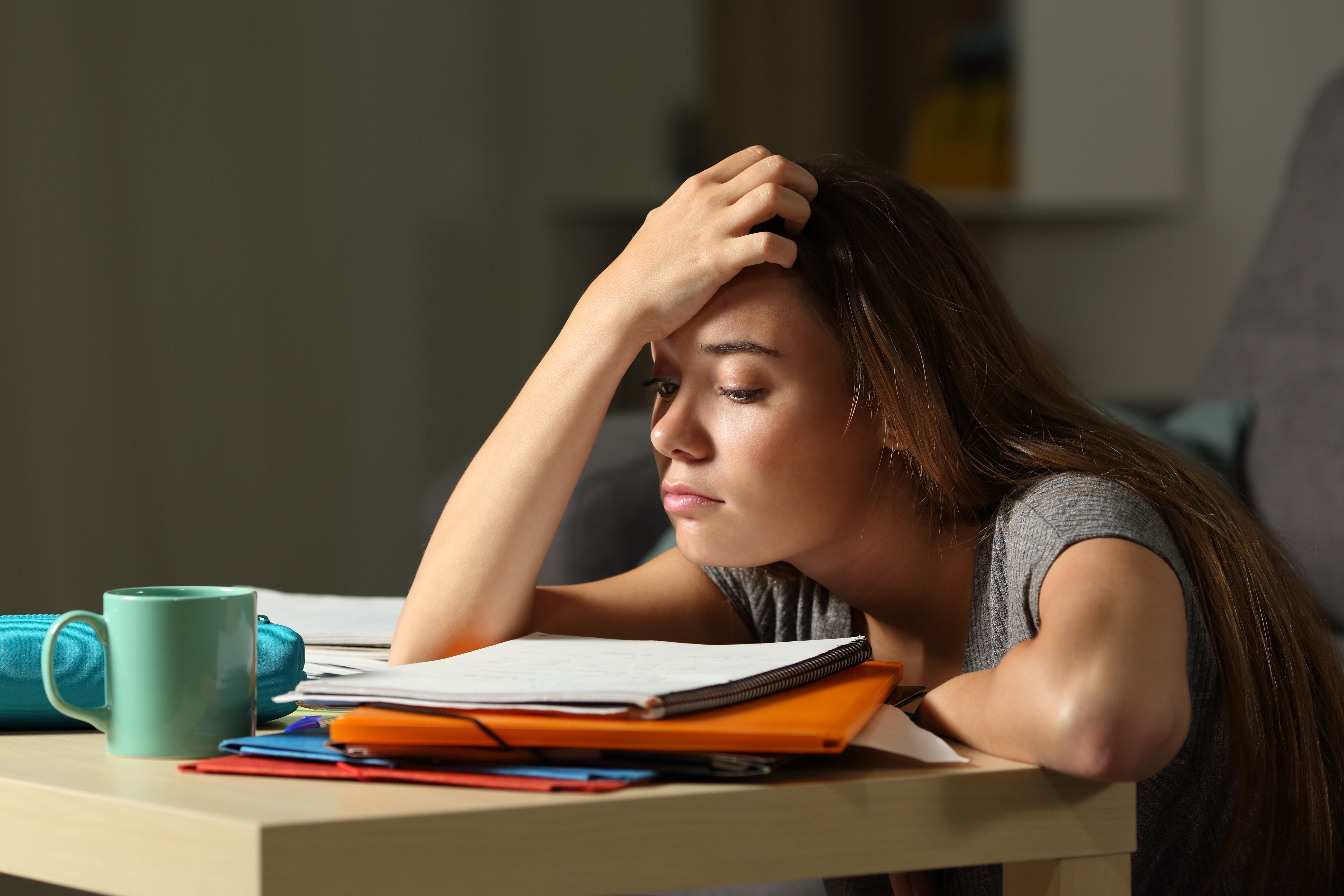 A person hunched over books at a desk, looking stressed.