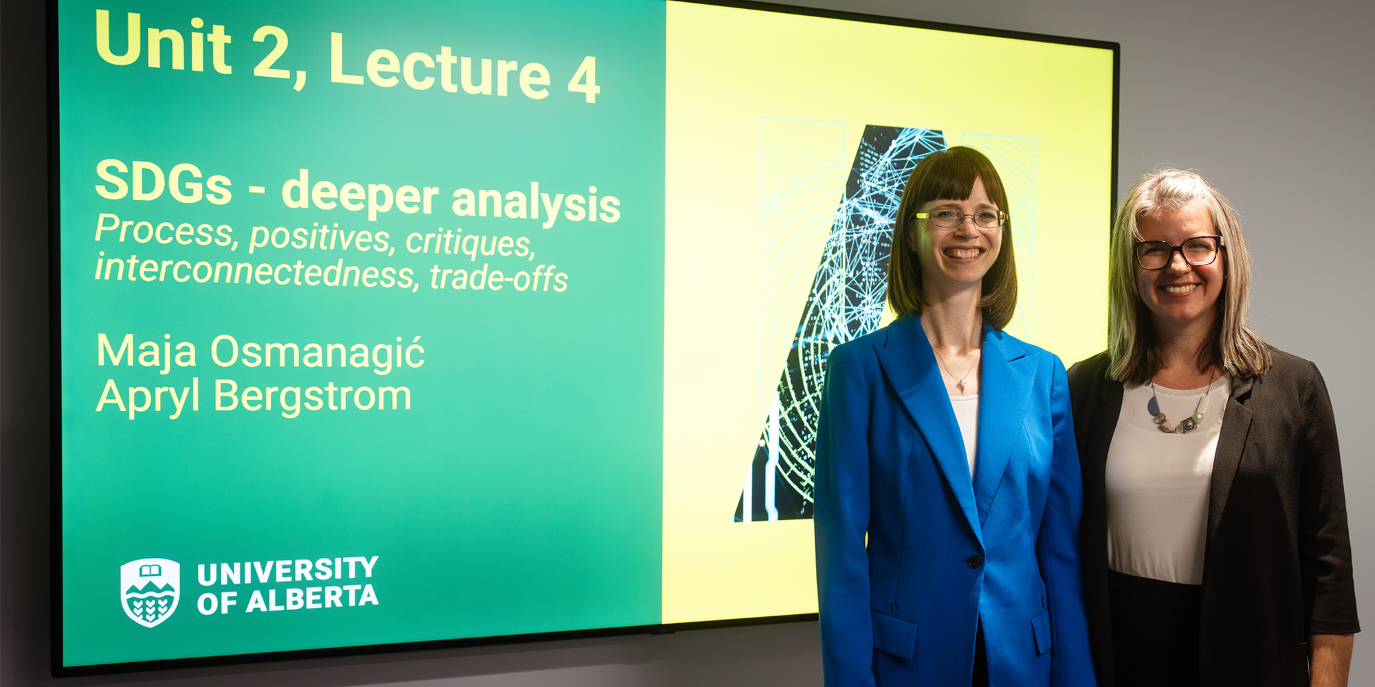 SUST 202 course instructors Maja Osmanagić and Apryl Bergstrom smiling while standing in front of a lecture slide presentation