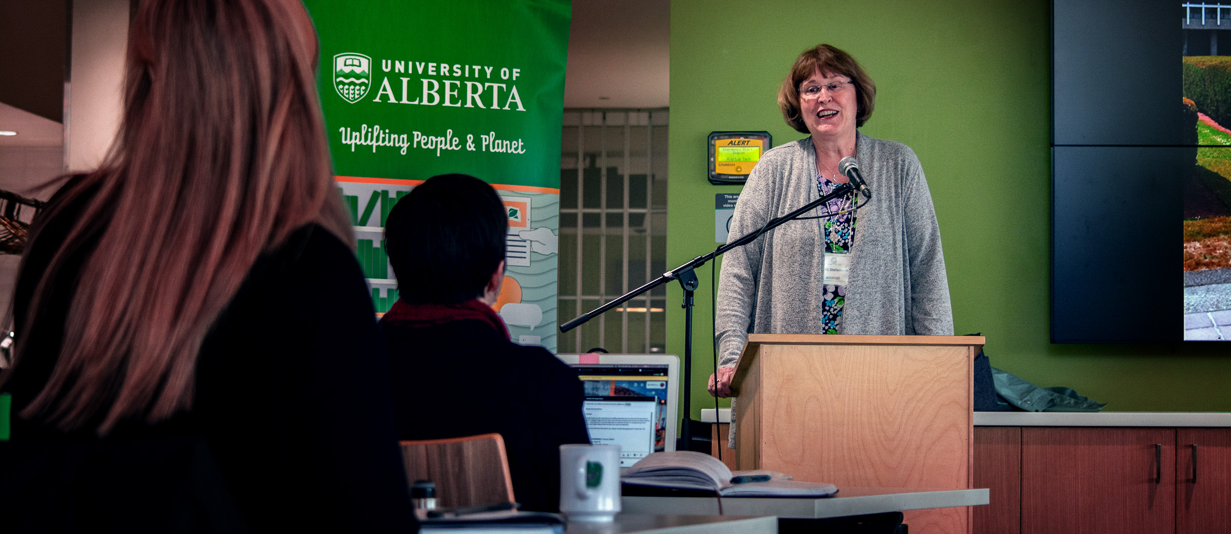 Woman speaks to audience beside Sustainability Council banner.