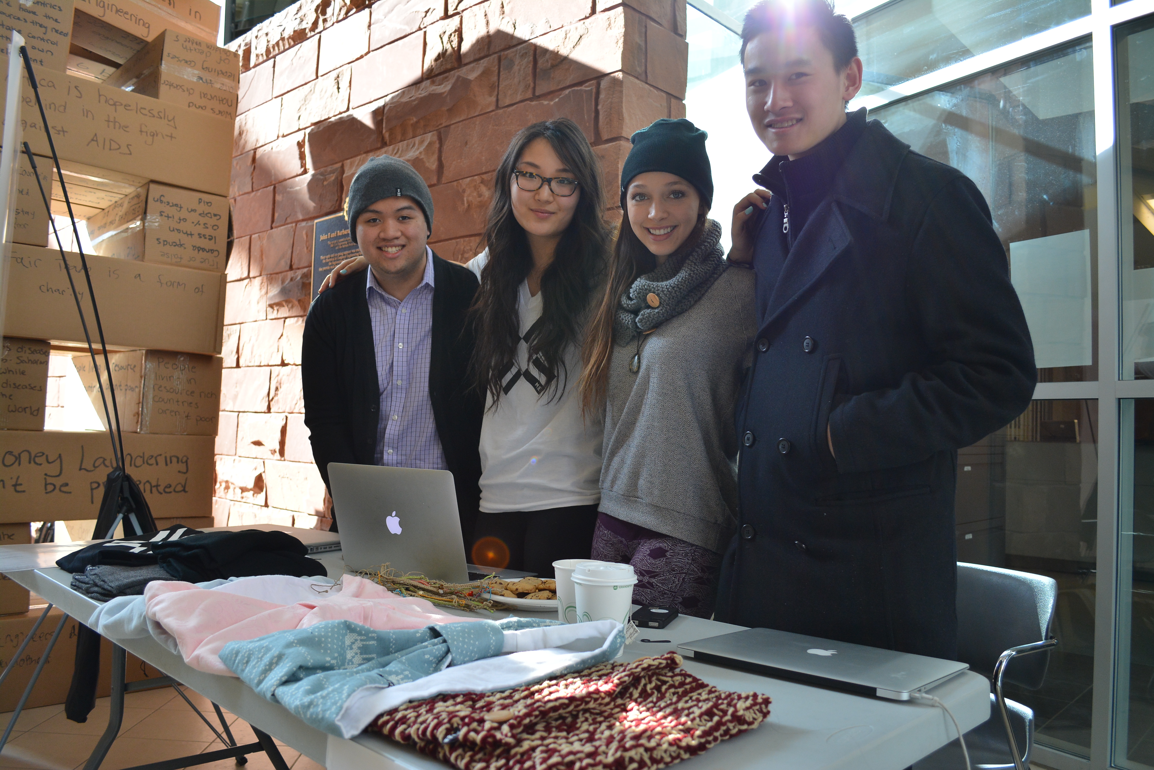 Young men and women standing behind table with hand-made goods.