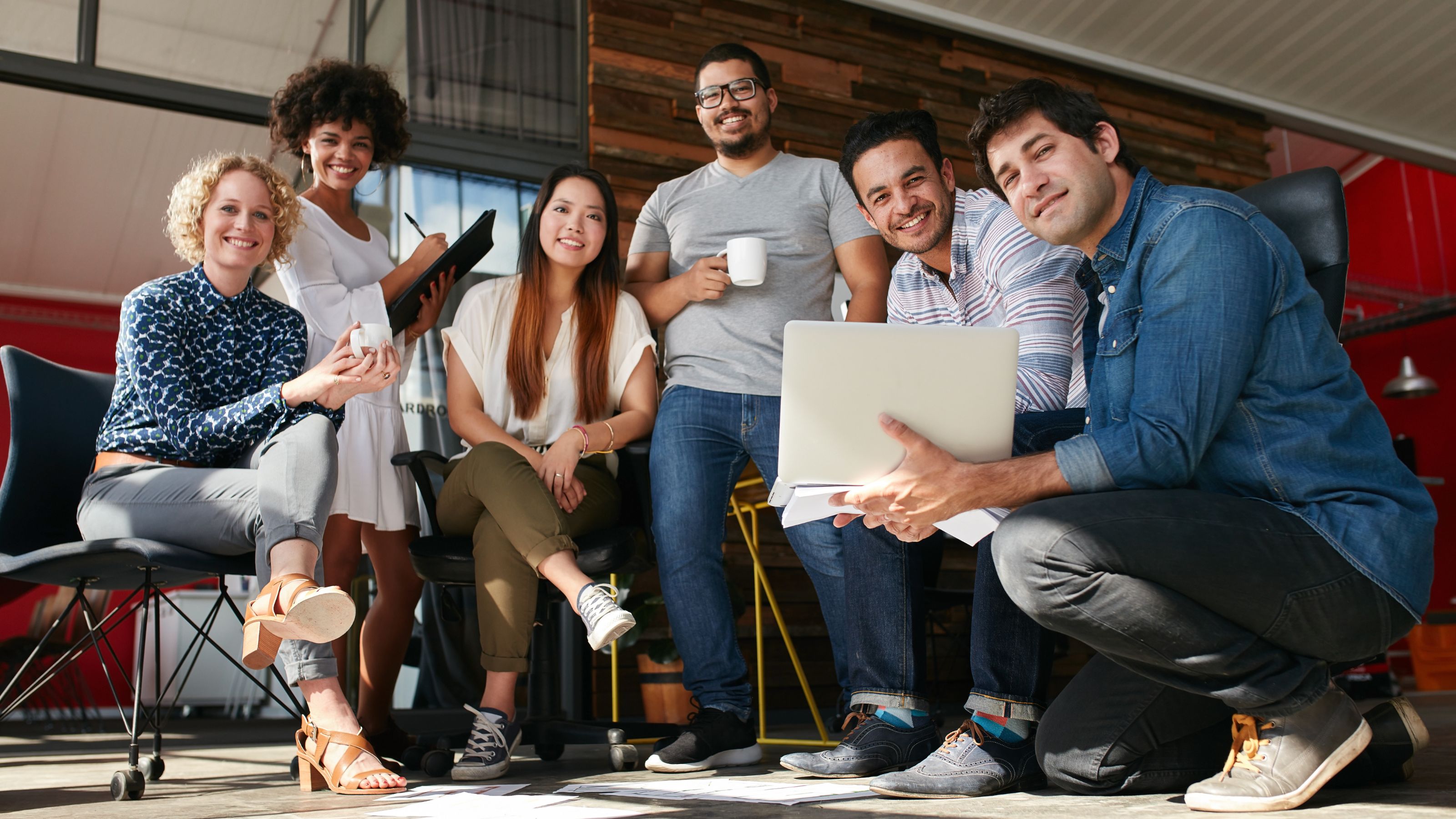 A group of five casually dressed people pose for a photo in an office