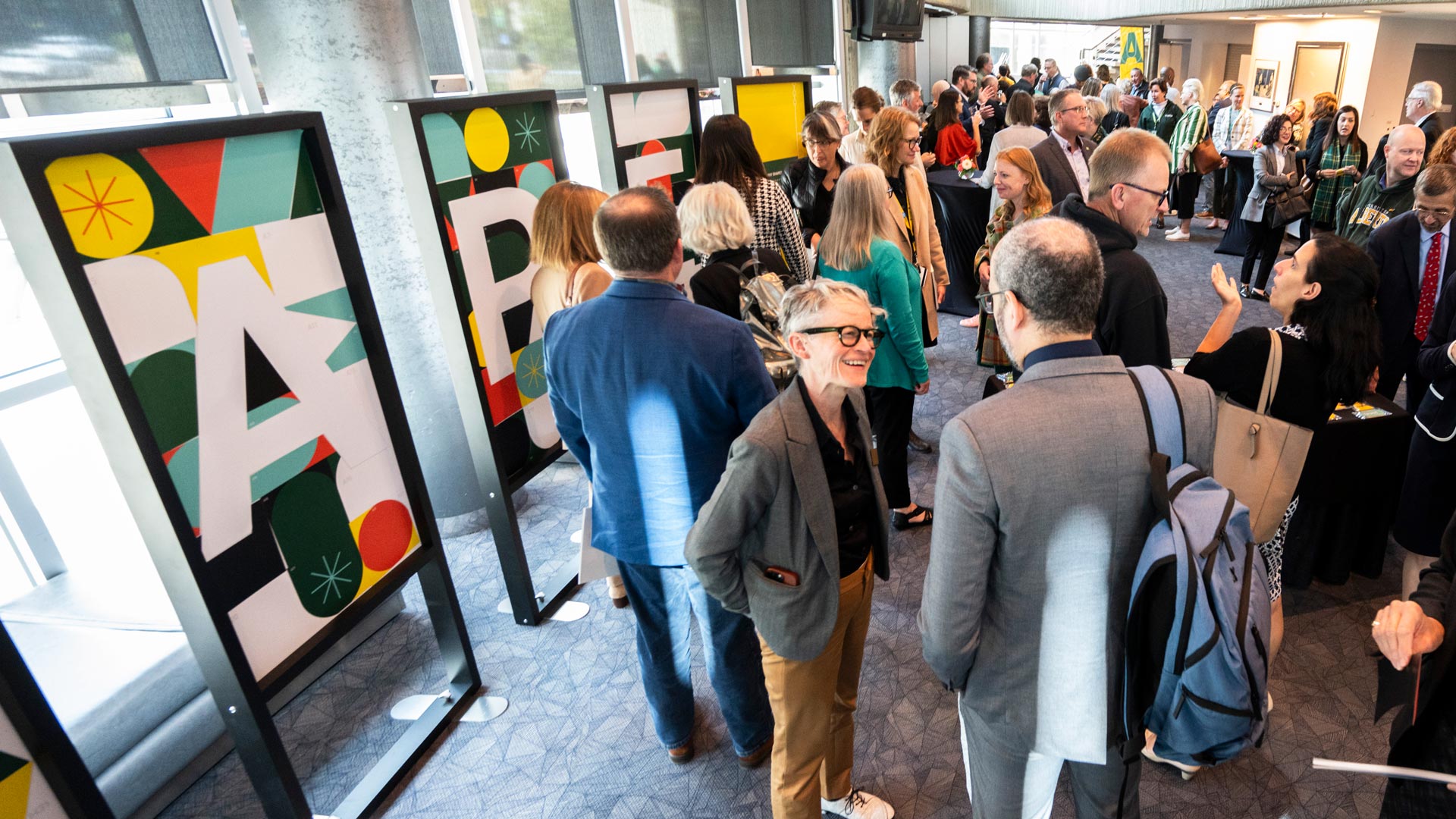 Members of the university community connect after the event in front of posters spelling the word Shape