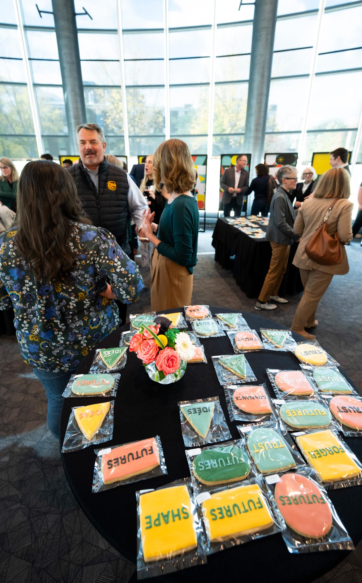 Members of the university community connect after the event in front of shaped cookies and posters spelling the word Shape