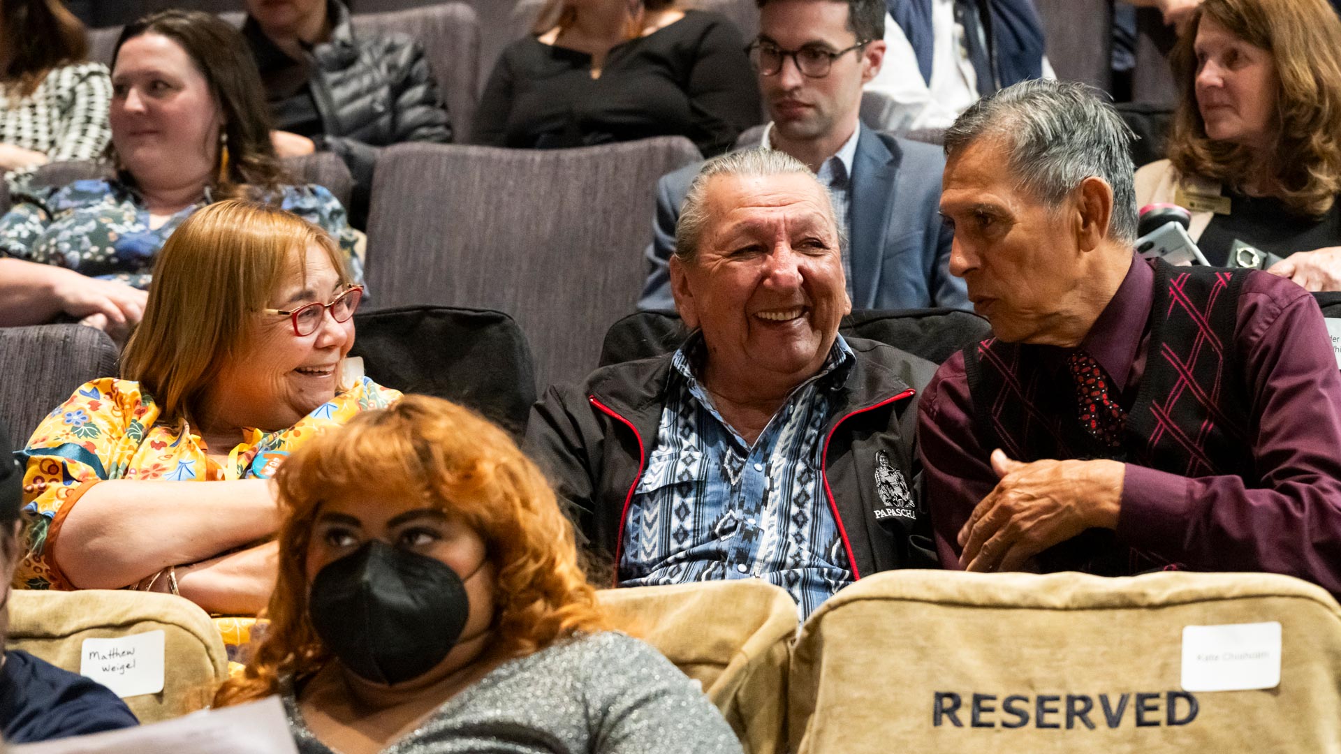 Florence Glanfield chats with two Elders in their seats before the event starts