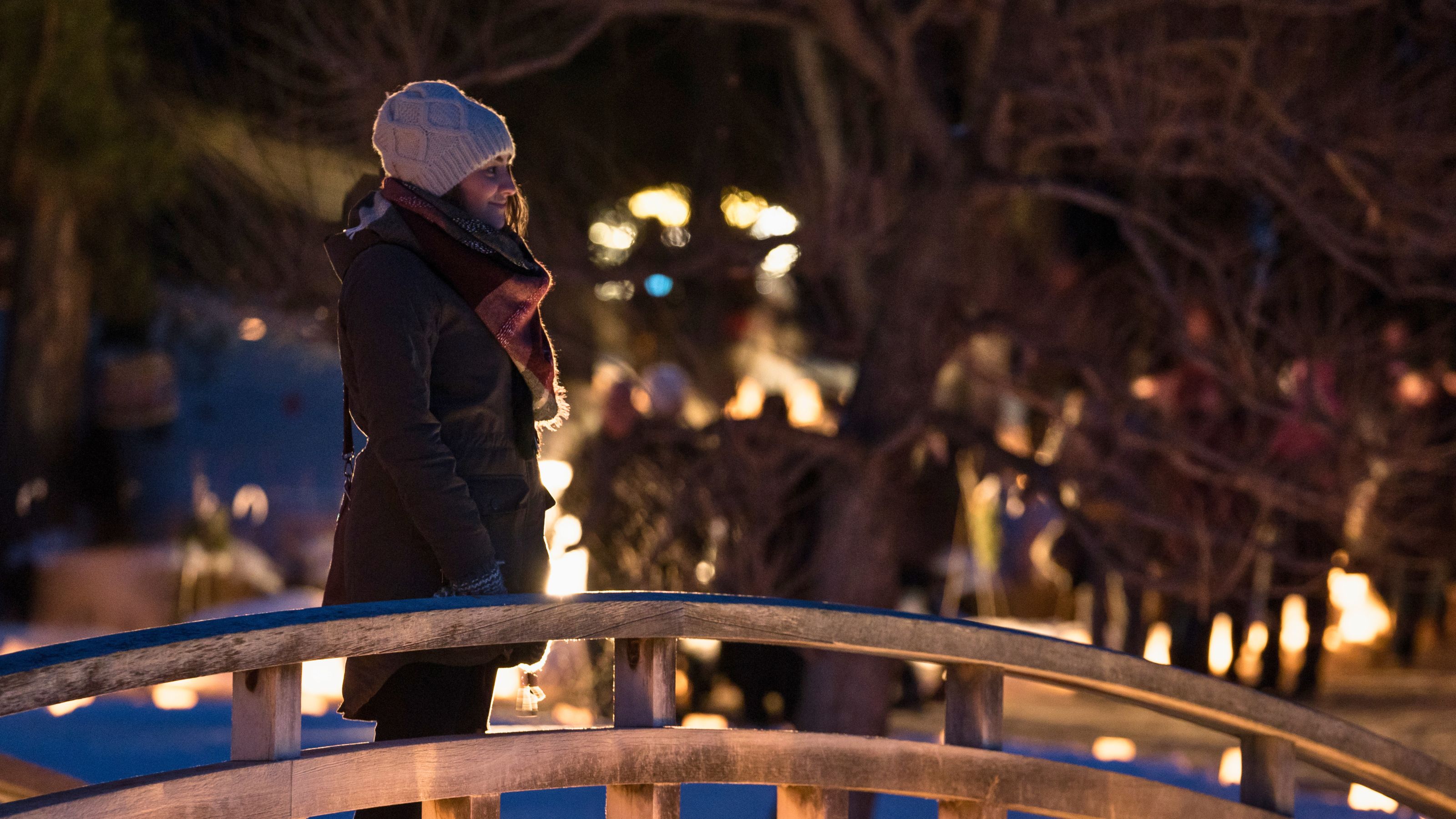 Woman at Lumanaria - on bridge in winter, bridge sides are lit up with several candles in paper bags.