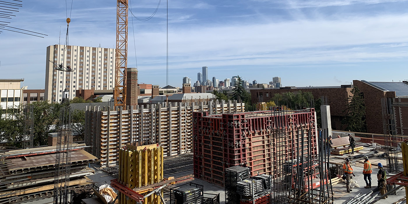 New building materials and construction workers on the roof of a building on campus