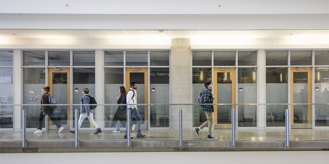 Students walking by a series of doors along a walkway