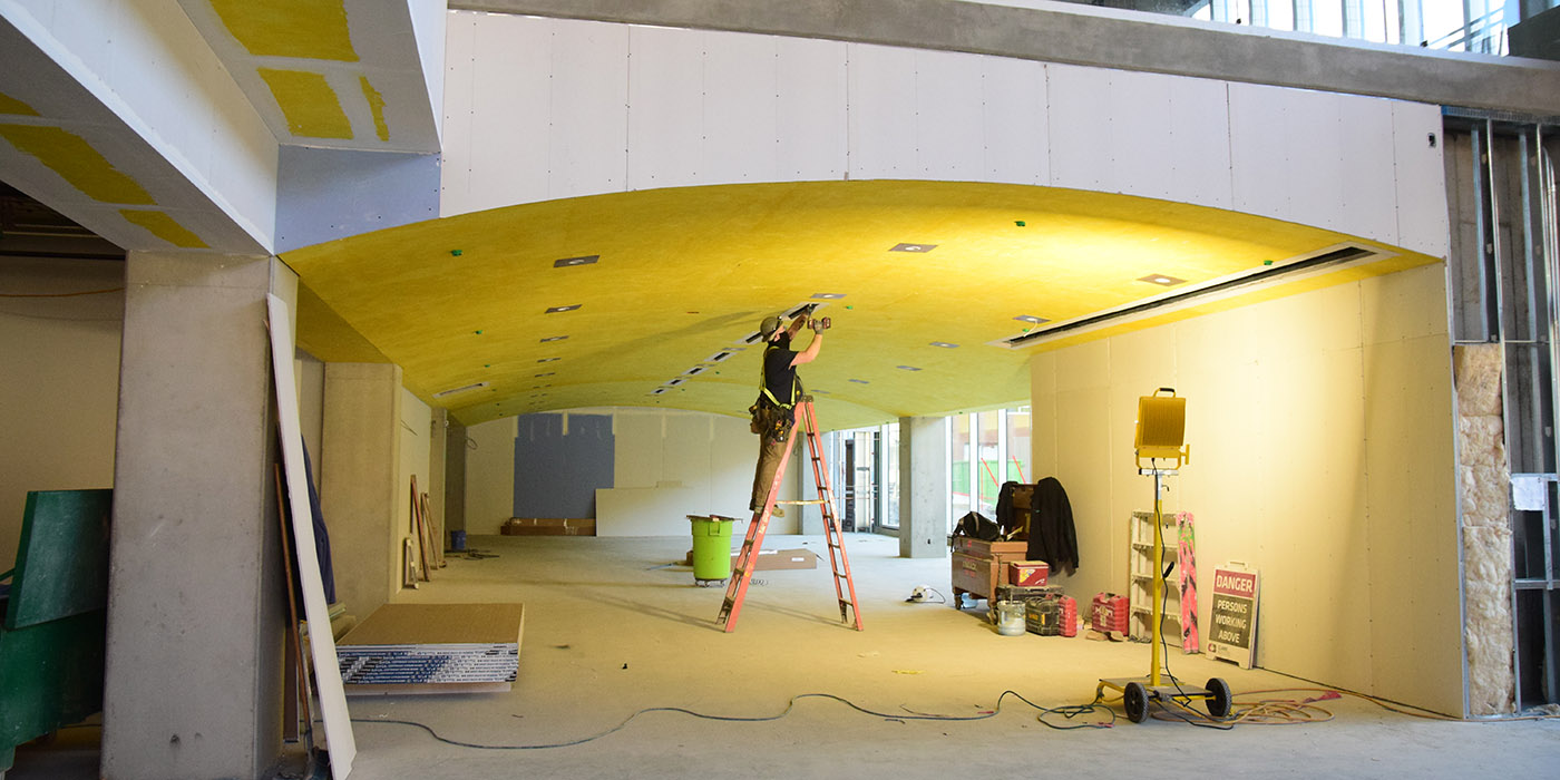 Builder on a ladder installing fixtures in a new hallway