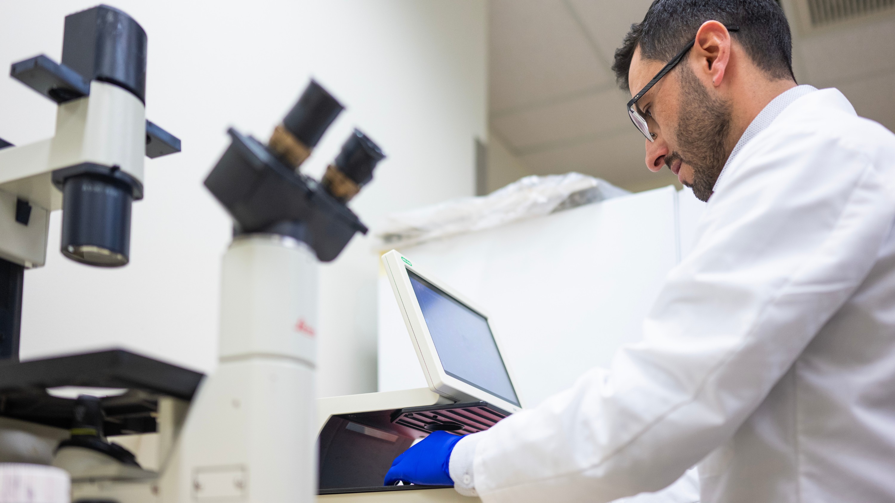 PhD grad Yasser Tabana examines a sample through a microscope in the lab. (Photo: John Ulan)
