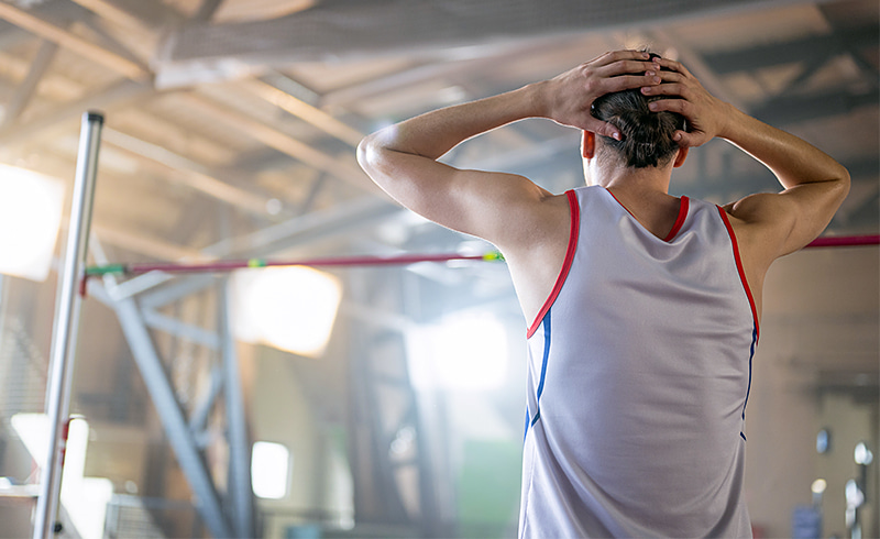 Back of athlete with hands on their head to exhibit stress of an impending high jump.