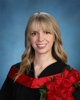 Taylor Tallent smiles at the camera against a blue backdrop, wearing a black graduation robe and holding a bouquet of red roses