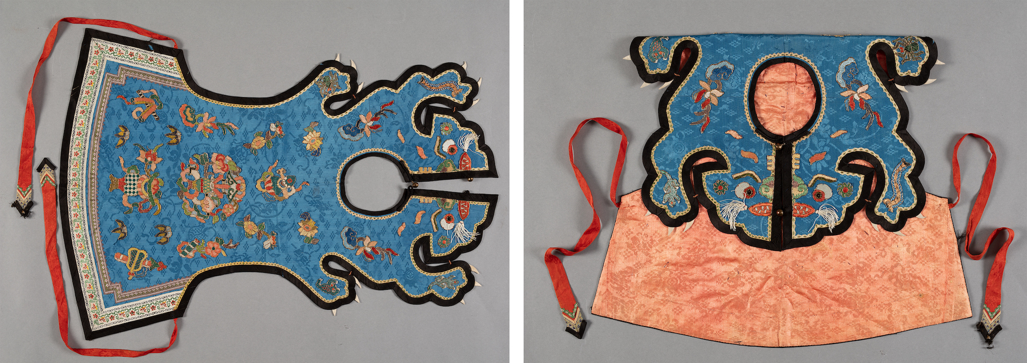 A blue bib covered in auspicious symbols laid flat. The top part of the bib that would go around a child’s neck is shaped like a tiger with paws, claws, eyes, and whiskers. 